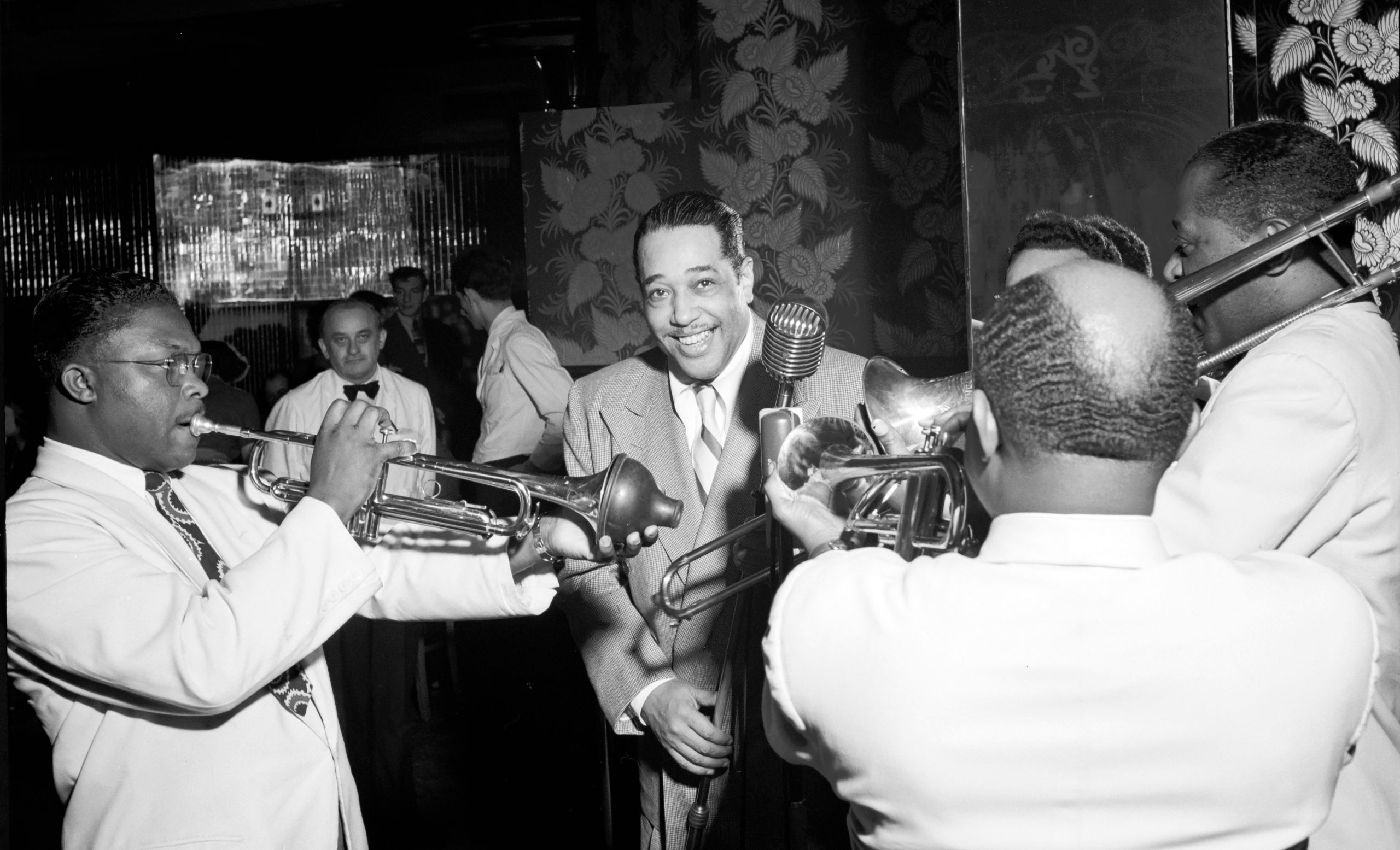 Duke Ellington surrounded by other musicians playing metals.
